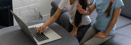 Two girls working on laptop, smiling and older sister help younger