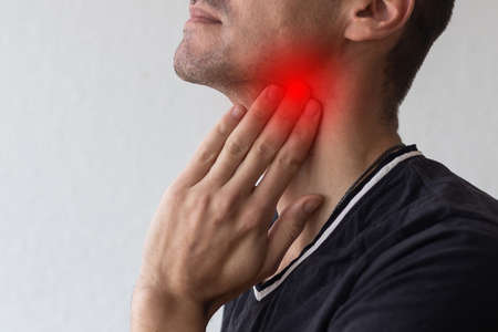 Man touching his neck, having a throat irritation on grey backgroundの写真素材