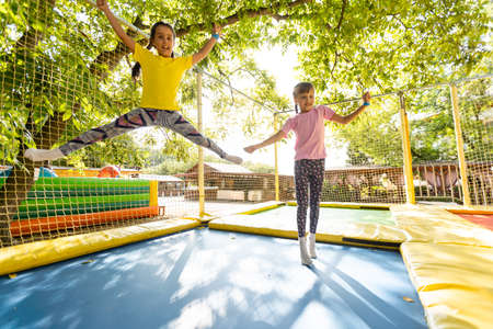 Two little girls in the summer jump on a trampoline, smiling and laughing. Children play. Relax in the fresh air. Friends jump on a trampoline. Happy childの写真素材