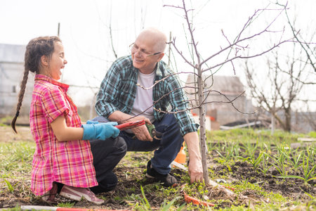 A small girl with grandfather outside in spring nature, having fun. gardening
