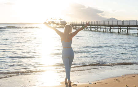 Side view of slim woman in sportive clothes walking near calm sea waves spending weekend morning for training at nature, beautiful female in tracksuit choosing place for stretchingの写真素材