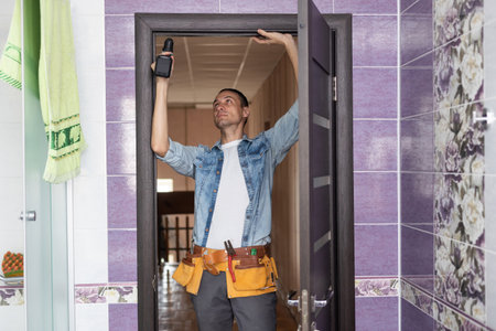 Young handyman installing a white door with an electric hand drill in a room.の写真素材