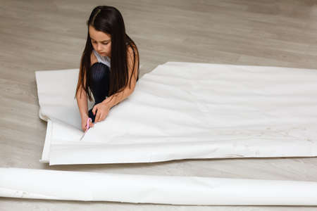 Little girl is cutting paper using scissors while sittingの写真素材