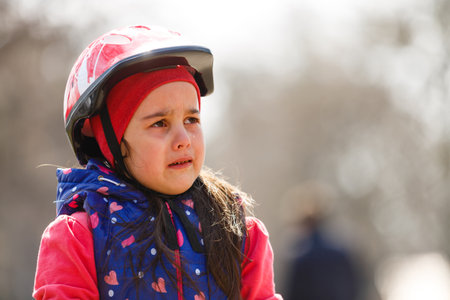 Beautiful brunette little girl wearing bike helmet and reflective vest with sad expression crying. depression concept.の写真素材