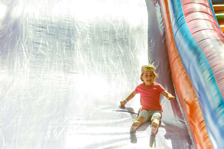 Happy little girl having lots of fun on a jumping castle during sliding.の写真素材