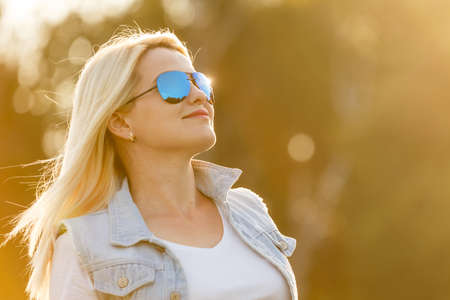 portrait of a young woman, blonde, sunglasses, outdoors in the park.の写真素材