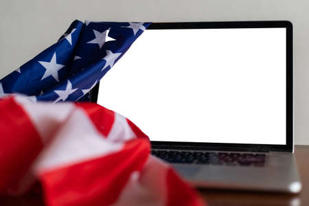 Laptop with blank screen and USA flag on desk in officeの写真素材