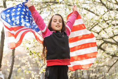 Happy adorable little girl smiling and waving American flag. Patriotic holiday. Happy kid, cute little child girl with American flag. USA celebrate 4th of July. Independence Day concept.の写真素材