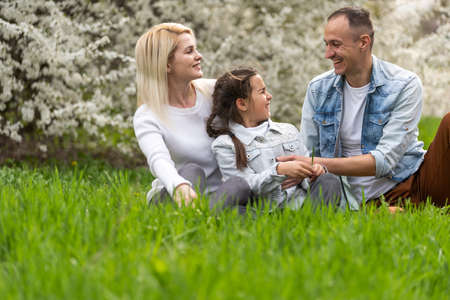 Outdoor portrait of happy young family playing in spring park under blooming tree, lovely family having fun in sunny gardenの写真素材