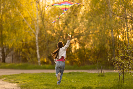 Happy little girl running with kite in hands on the beautiful field at sunrishe time