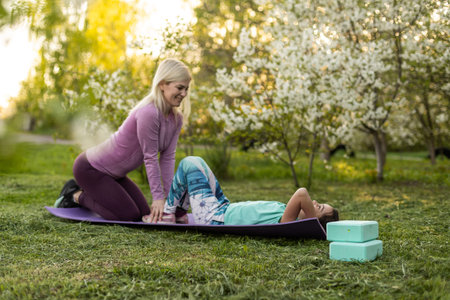 Young sports mother doing physics exercise outdoors in garden near her daughter. Healthy lifestyle....