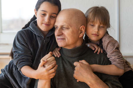 grandfather and two granddaughters hugging on sofa at homeの写真素材