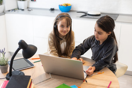 Two child girl students study online with teacher by video call together. Siblings are homeschooling...