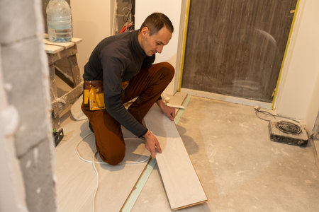 Repairman laying laminate flooring at home.