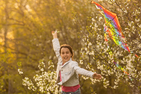 Happy child playing with colorful kite outdoors. Kid having fun in green spring field. Freedom and...