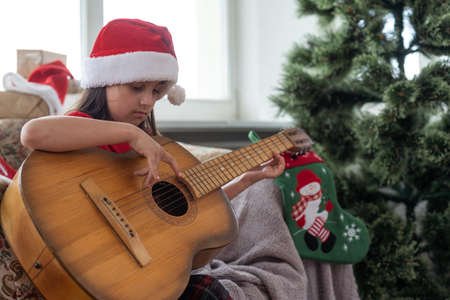Child playing the guitar and singing near christmas treeの写真素材