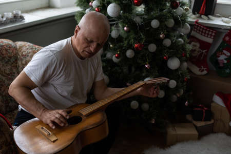 Happy people family concept - Old senior man enjoying the guitar on the sofa in the house at christmasの写真素材