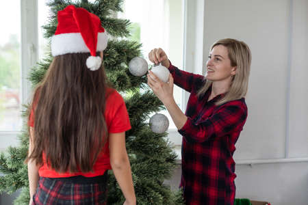 Mother and children decorating the house hang Christmas tree toys on the Christmas tree in a large wooden houseの写真素材