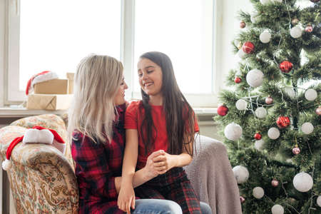 Merry Christmas and Happy Holidays. Mom and daughter decorate the Christmas tree indoors. The morning before Xmas. Portrait loving family close upの写真素材