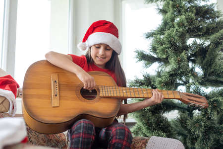 Child playing the guitar and singing near christmas treeの写真素材