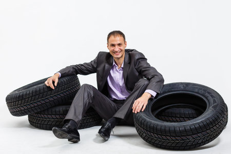 Full length portrait of a young businessman leaning on a pile of car tires isolated on white...