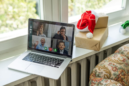 A happy family with a child is celebrating Christmas with their friends on video call using webcam. Family greeting their relatives on Christmas eve online. New normal virtual event.の写真素材