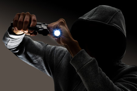 burglary and robbery. skillful professional masked burglar holding a gun and torch and breaking into...