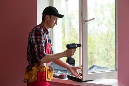 Construction worker repairing plastic window with screwdriver indoors, closeup.の写真素材