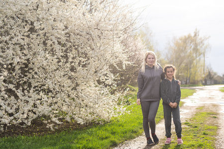 Woman walking with daughter in blooming spring garden exploring flowering tree. Family admires...