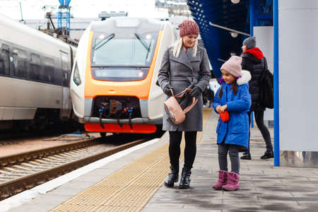 Yound woman and little girl, lovely daughter, on a railway station. Kid and woman waiting for train and happy about a journey. People, travel, family, lifestyle conceptの写真素材