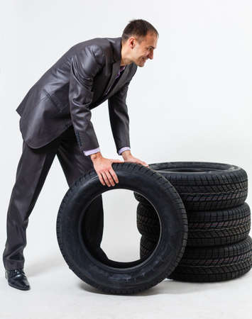 Full length portrait of a young businessman leaning on a pile of car tires isolated on white backgroundの写真素材