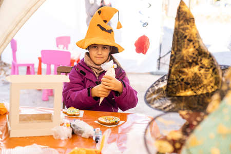 Little girl in Halloween costume plays with gingerbread cookies like a pumpkinの写真素材