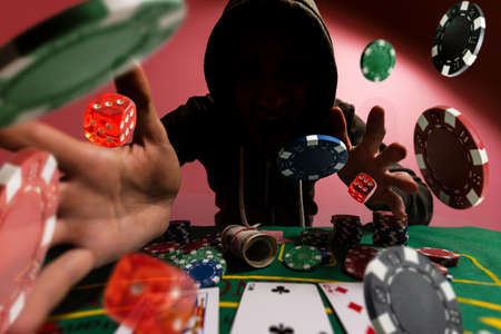 happy young attractive man grabbing and protecting poker chips with his hands after winning bet gambling at Casino with chips flying all around isolated on black background.の写真素材