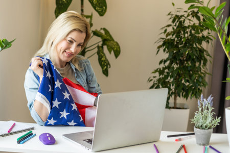 Happy woman employee sitting wrapped in USA flag, shouting for joy in office workplace, celebrating...