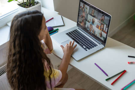 Home schooling. A girl is sitting at a table with a laptop during an online video chat of a school lesson with a teacher and class. Concept of distance education. Self-isolation in quarantine.の写真素材