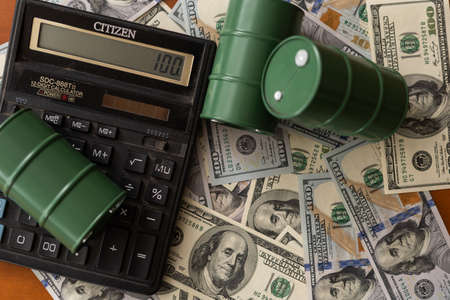 barrels with oil, a calculator against the background of dollar bills. oil business.の写真素材
