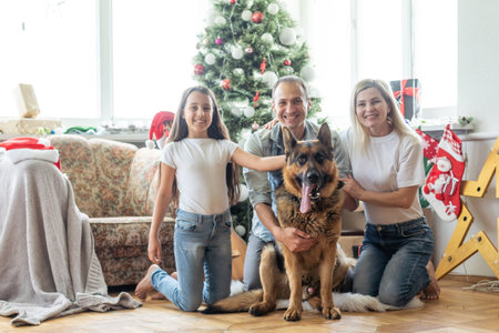 Friendly family is playing with dog near Christmas tree. They are sitting and laughingの写真素材