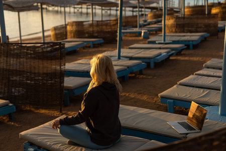 A calm woman sits on a sun lounger near the sea, gets distracted from working at the computer,...