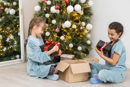 Two cute little girls under Christmas tree. Children under Christmas tree with gift boxes. New Years decorations. Sistersの写真素材