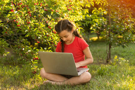 Beautiful young lady is chatting with friends outdoors as it is very useful to be in nature. Laptop is the best friend for a child nowadays. Green and vast meadowの写真素材