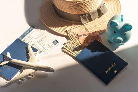 Save your money for travel. Piggy bank with coins, airplane and financial documents on a white desk.の写真素材