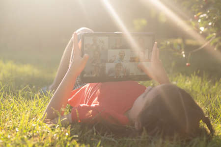 Girl on the grass with a tablet chat in her hands in the gardenの写真素材