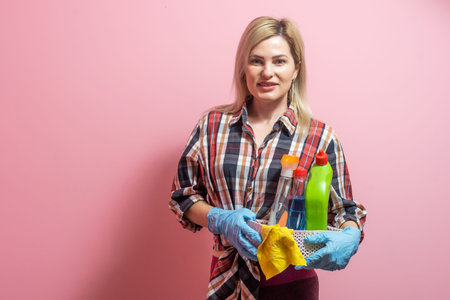 Photo of smiling young woman housewife in gloves holding cleanser bottles