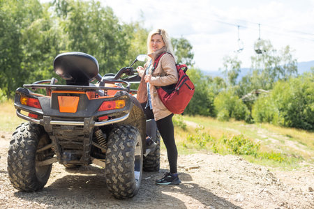 Smiling happy woman riding quad bike on a sunny day, against blue sky. Low angle shot. Freedom,...