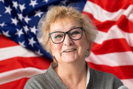 Old woman holds US flag on pink background. Concept patriot, holiday, independence day, memorial...