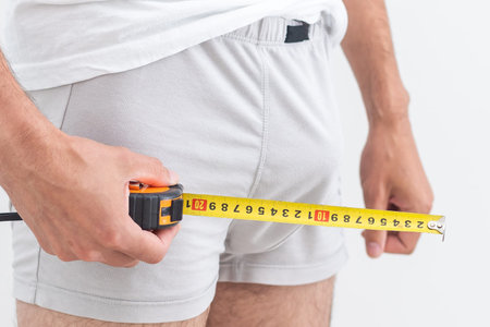 Young man holding tape measure, measuring his penis - focused at the middle of tape measure.の写真素材
