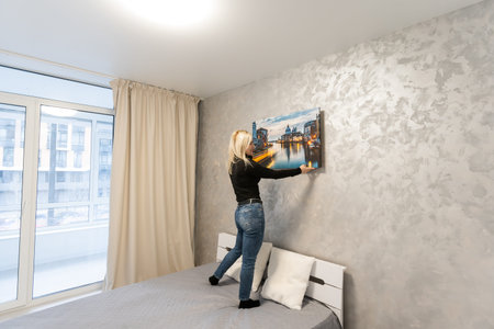 Canvas print with gallery wrap. Woman hangs photography on white wall. Hands holding photo canvas...