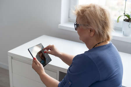 telemedicine concept, old woman with tablet pc during an online consultation with her doctor in her living room.の写真素材