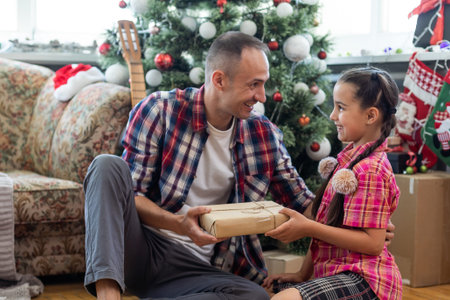 Little four year girl with her dad in living room decorated by Christmas tree and present gift box,...