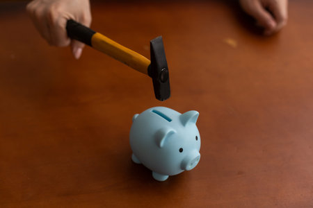 Man breaking piggy bank with hammer on tableの写真素材